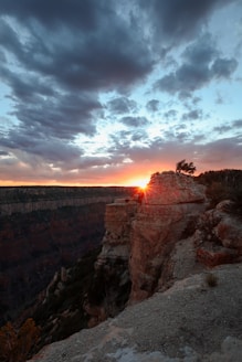 The sun is setting at the edge of a cliff