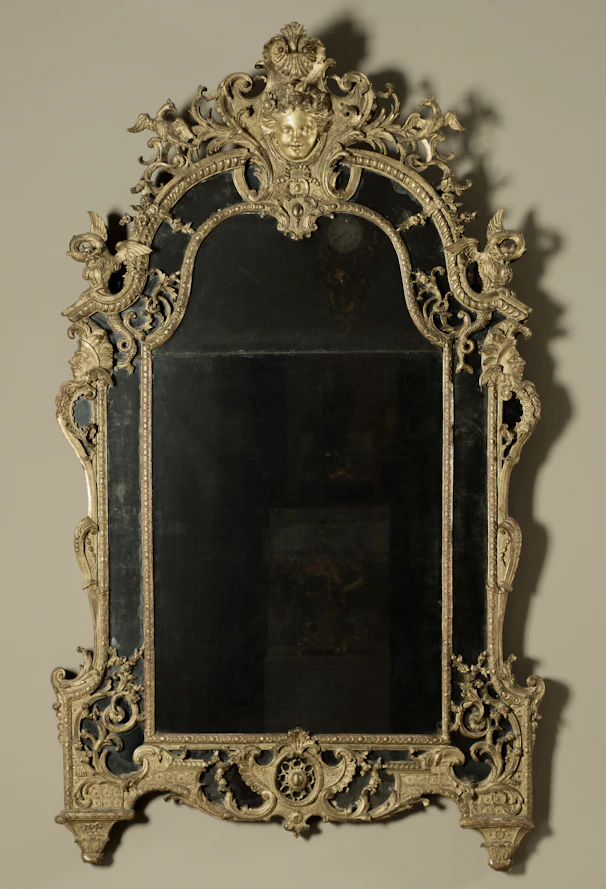 Ornate gilded mirror with intricate scrollwork and figural details.