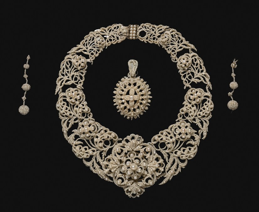 Une parure ancienne de perles fines sur nacre, collier, pendentif et boucles d’oreilles, posée sur un fond sombre