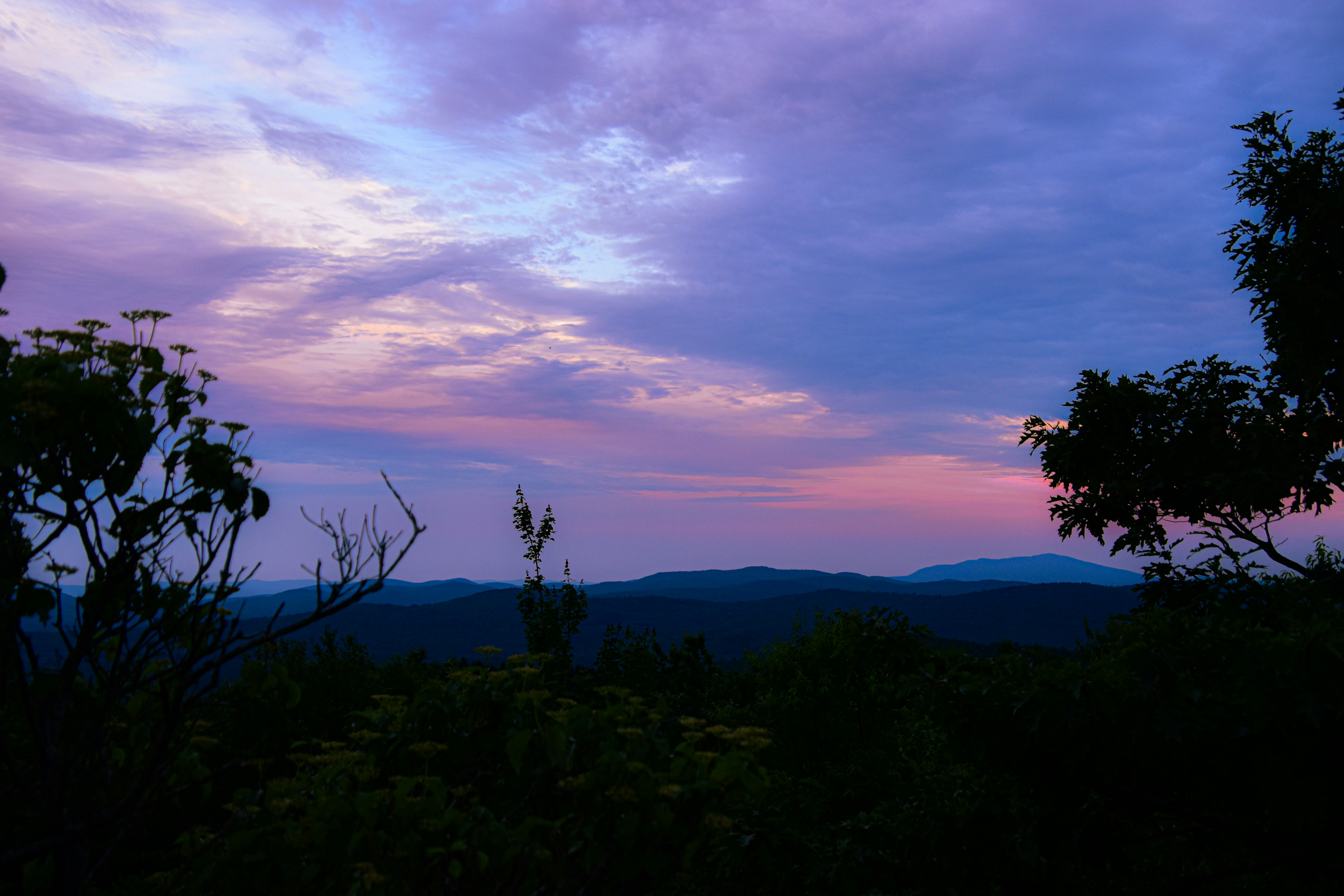 A purple and blue sky with clouds and trees