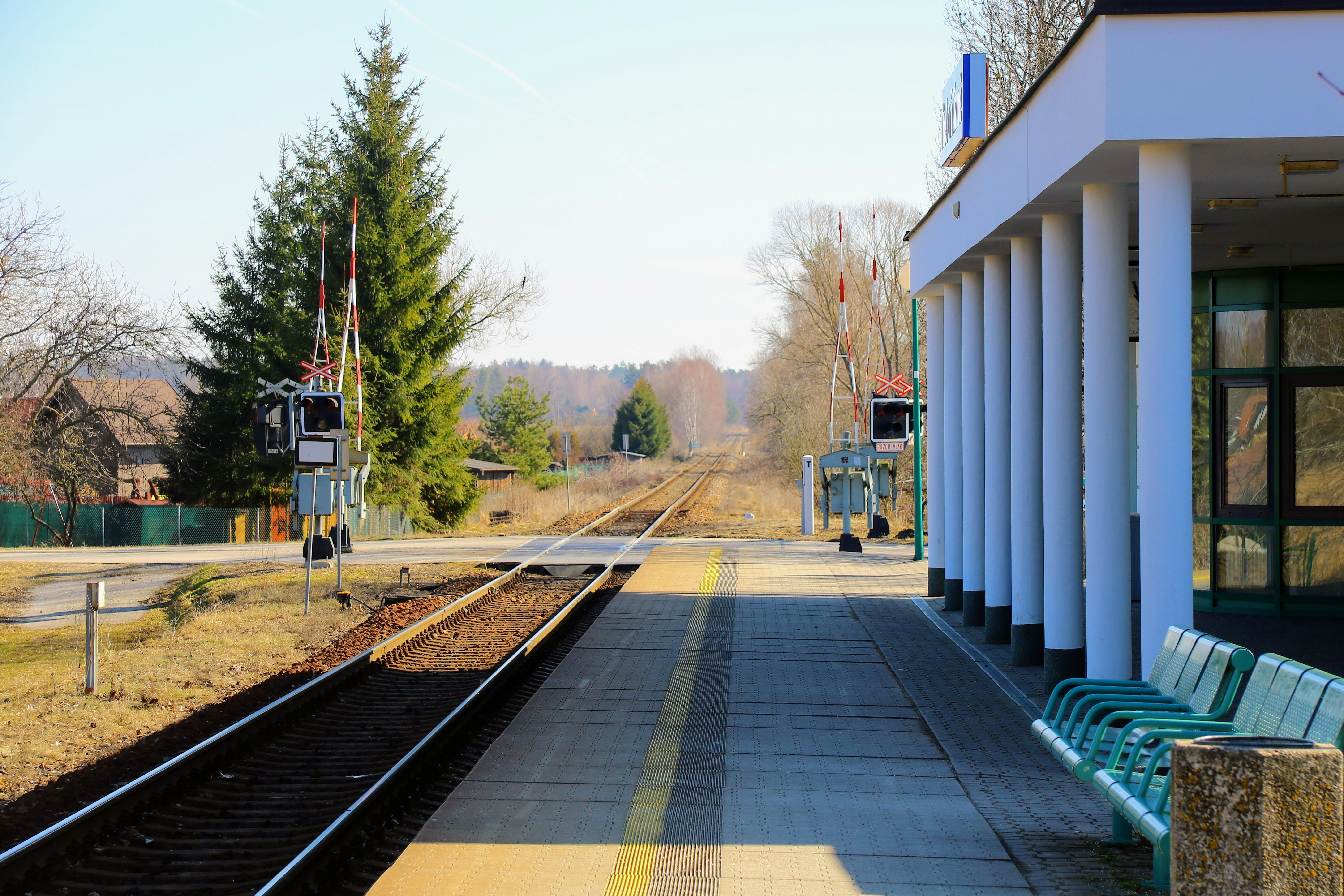 A bench sitting on the side of a train track, A rural train station platform with minimalistic design, surrounded by nature, waiting for passengers and trains.