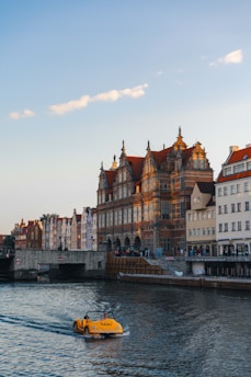 A yellow boat traveling down a river next to tall buildings