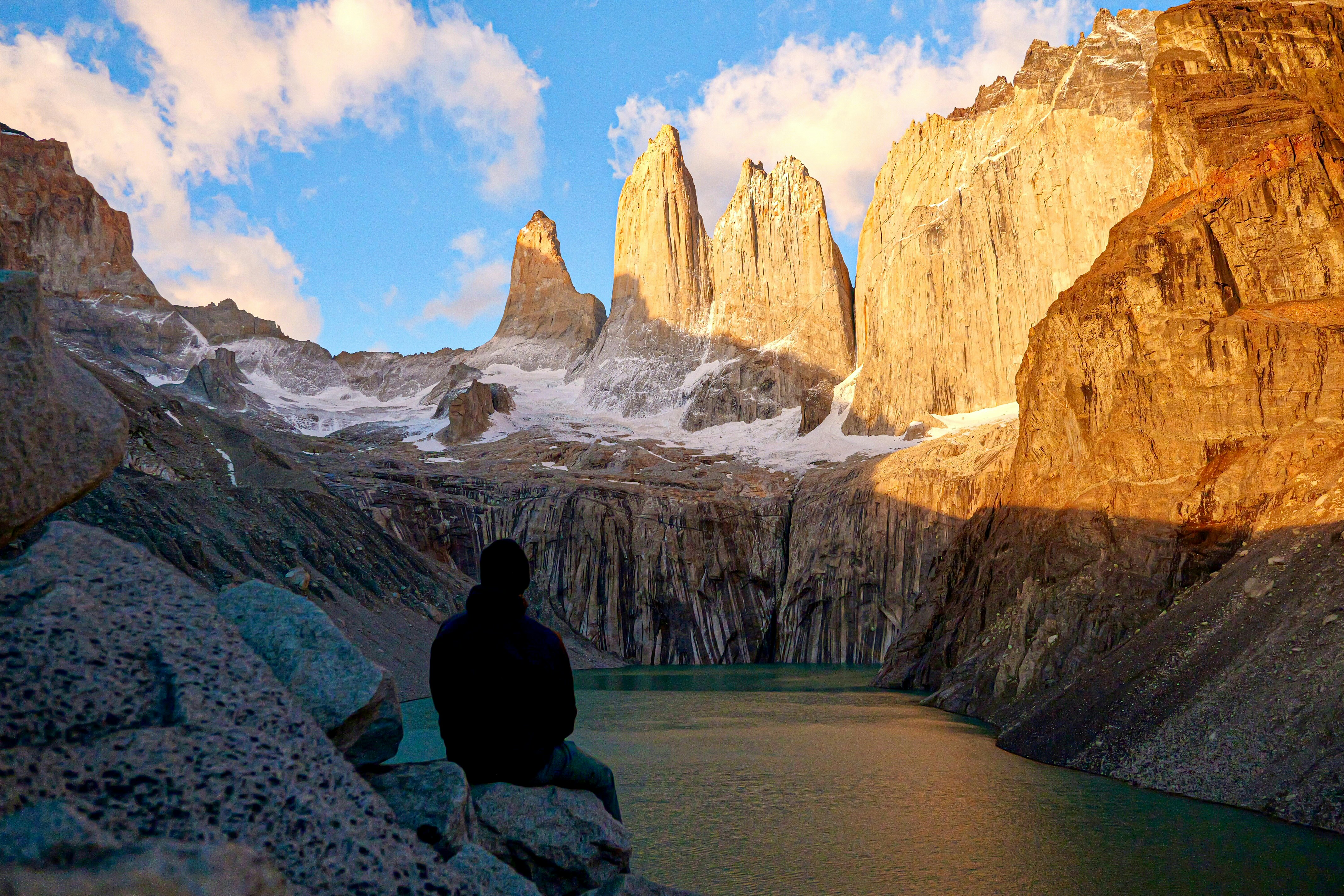 A man sitting on a rock looking at the mountains, Golden sunrise at Mirador Las Torres in Torres Del Paine National Park, Chile.