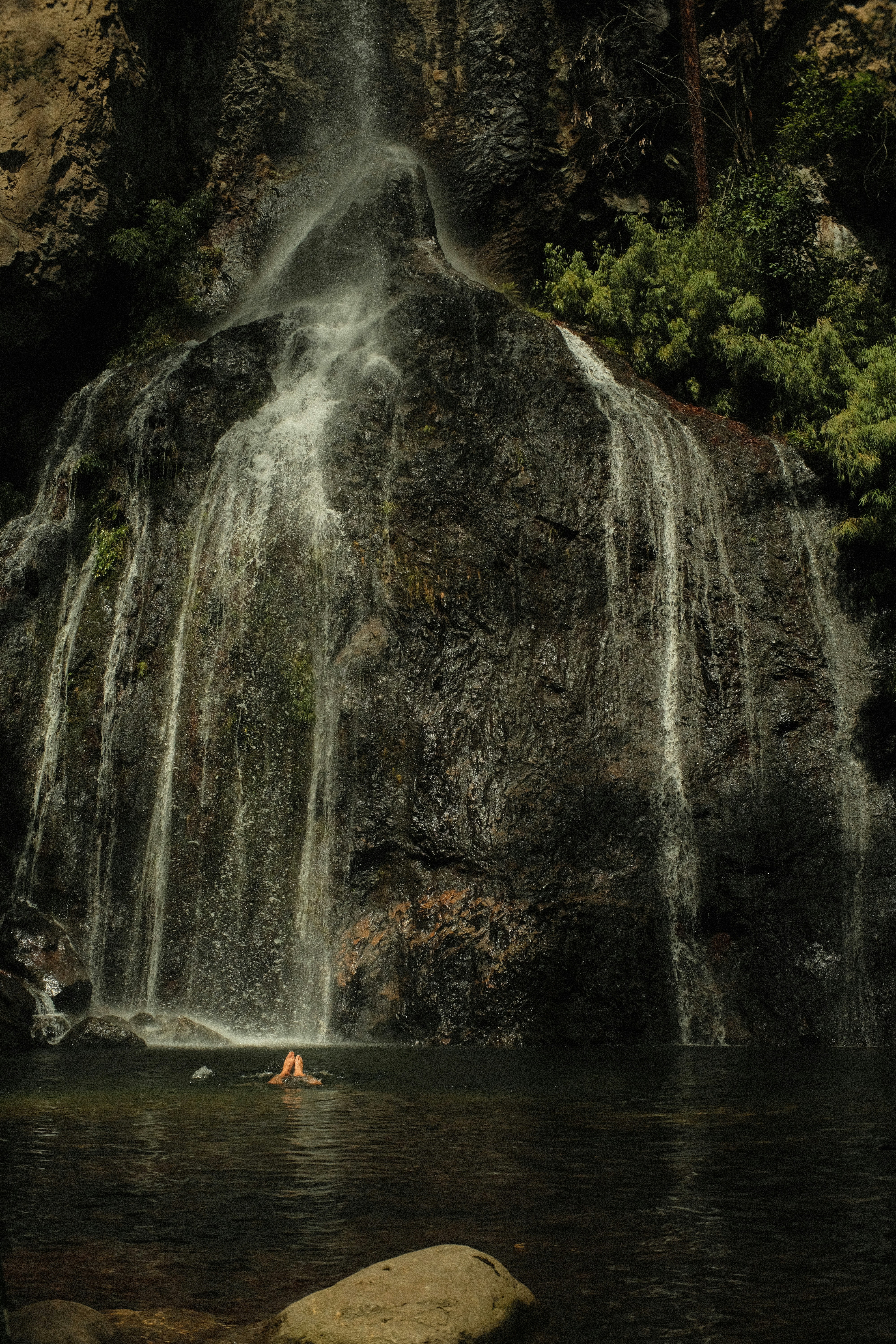 A person swimming in a body of water under a waterfall