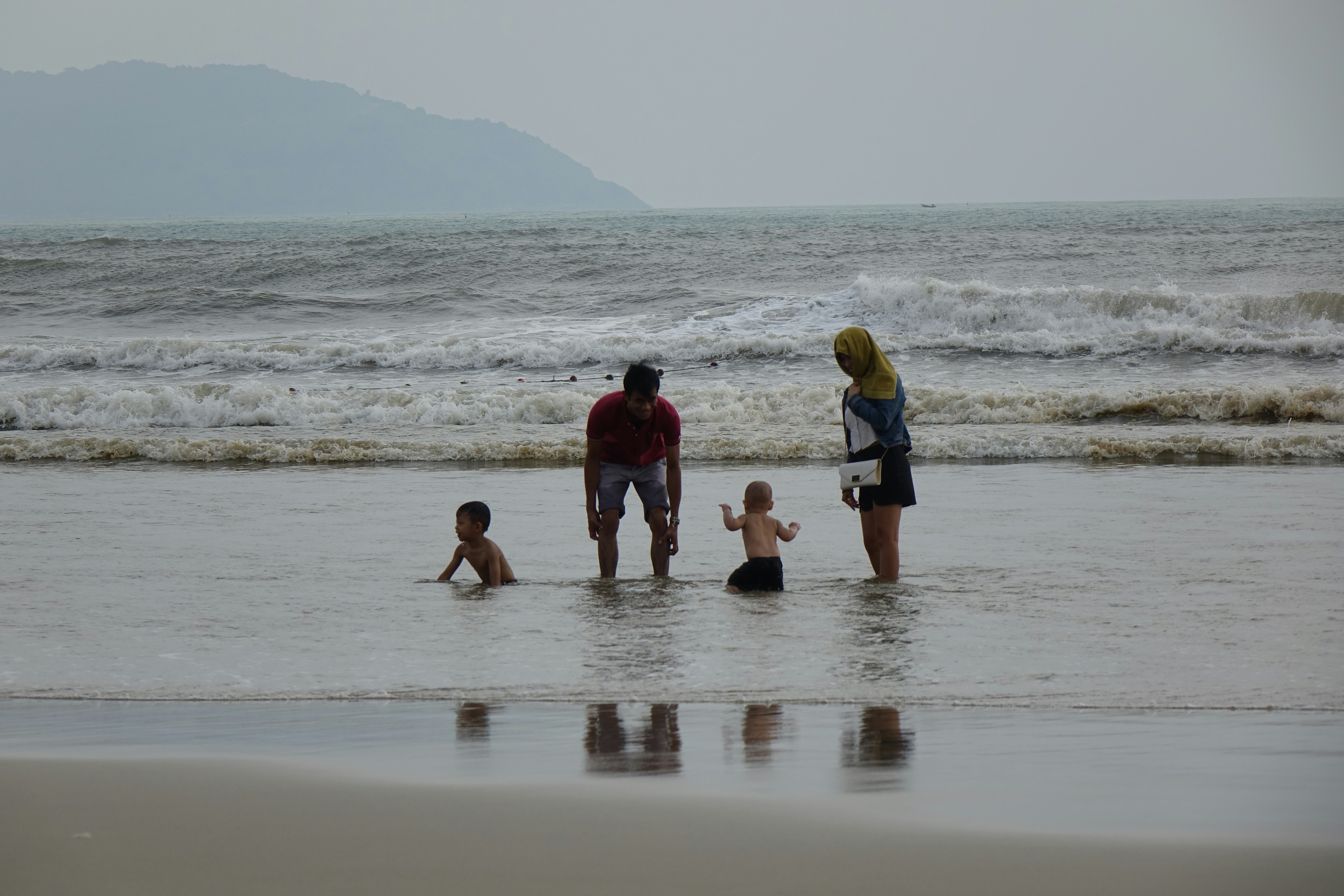 A group of people standing on top of a beach next to the ocean, 