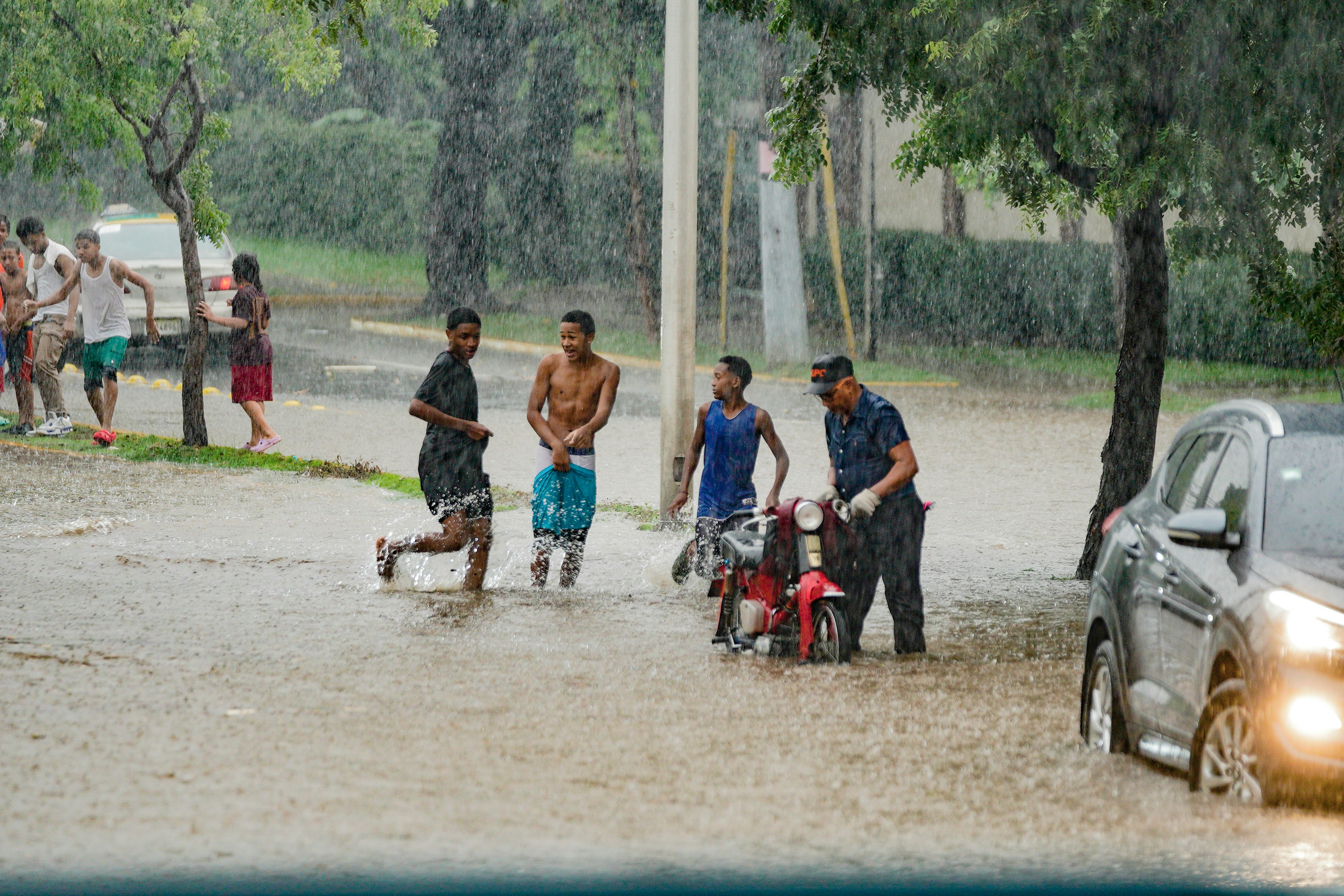 Two children splashing in flooded road after monsoon rain, pure joy, backlit by afternoon sun