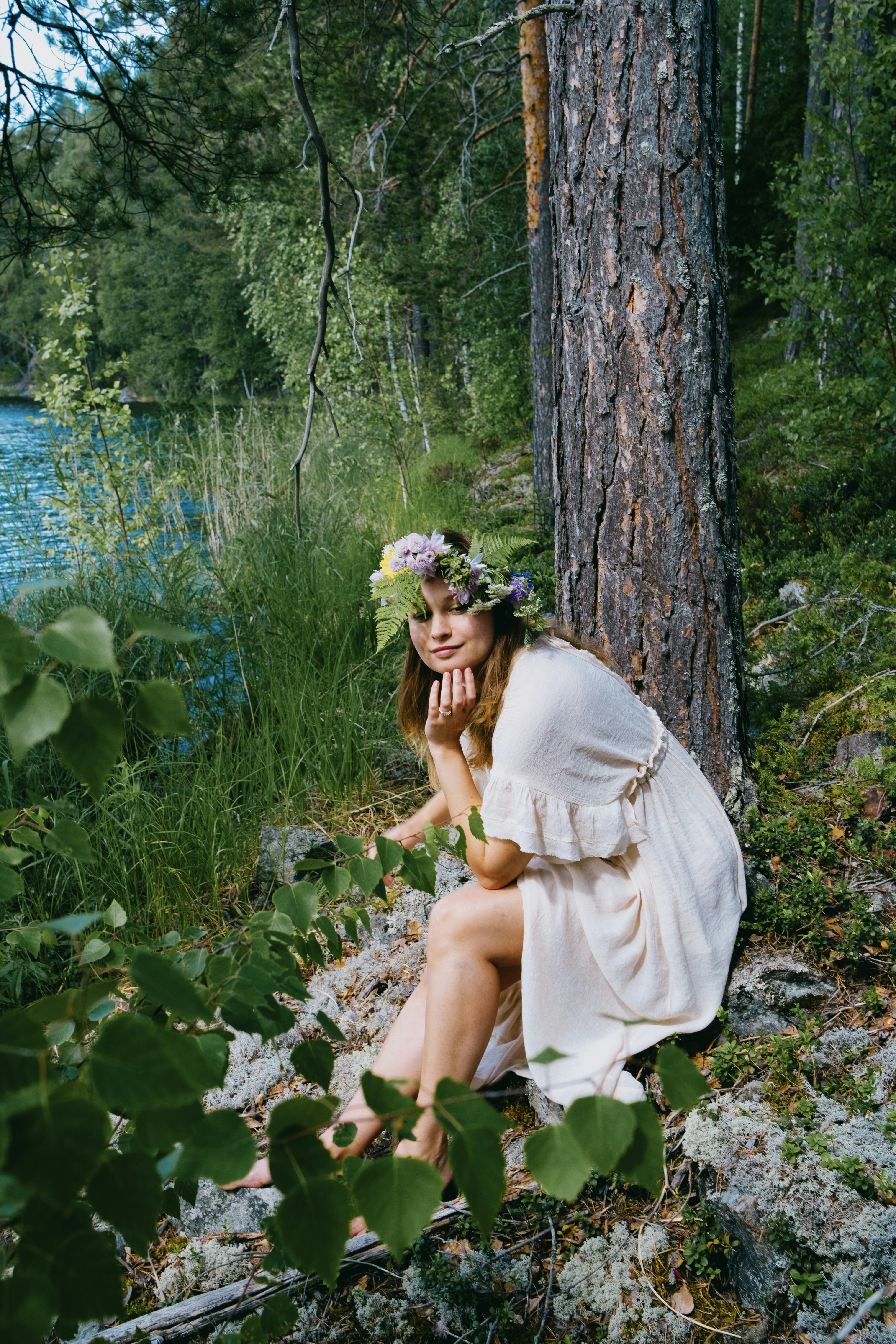 Eine Frau in einem weißen Kleid sitzt neben einem Baum