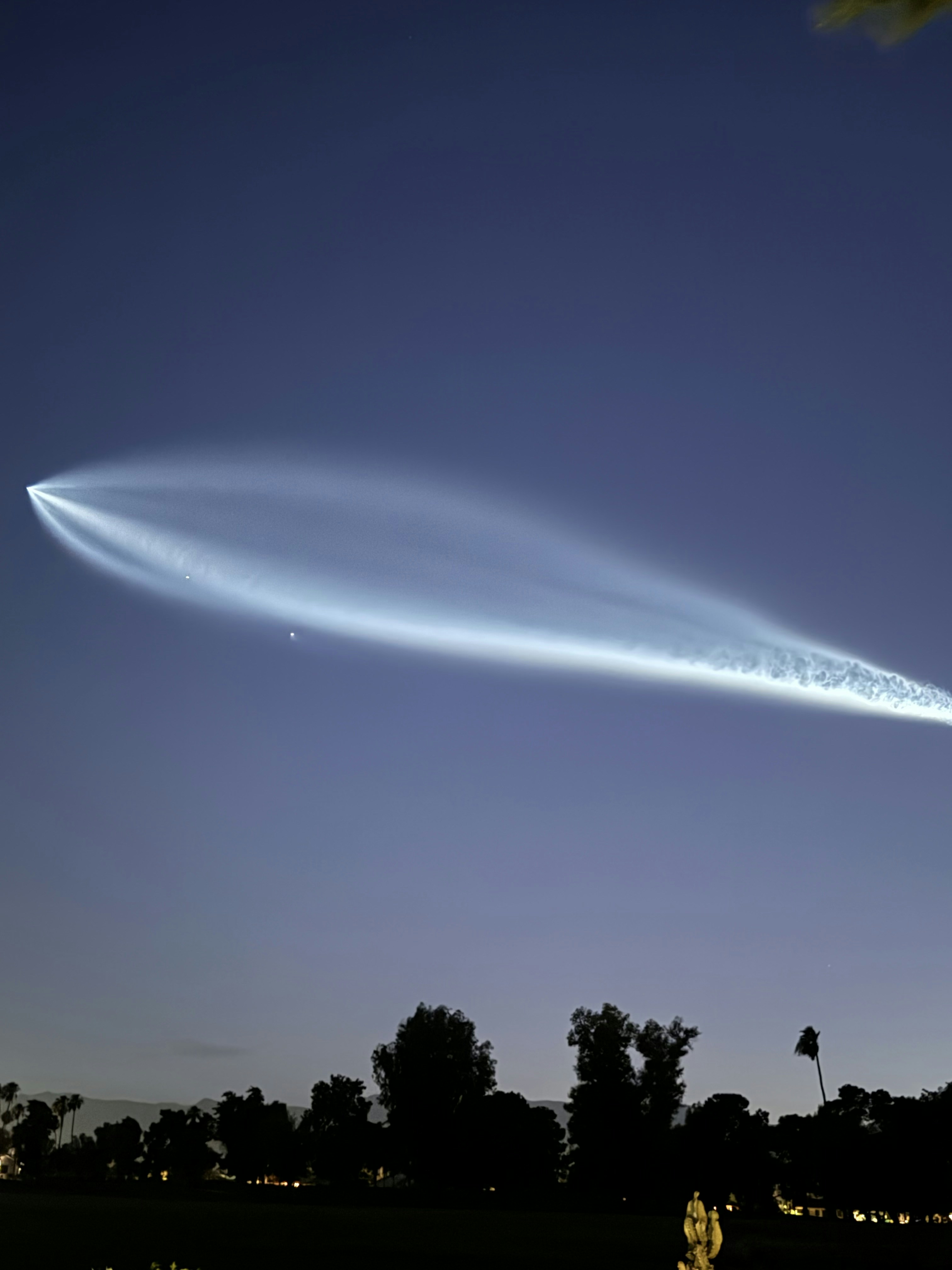 A contrail is seen in the sky over a park