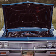 A blue car with its hood open in a field