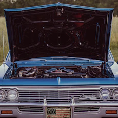 A blue car with its hood open in a field