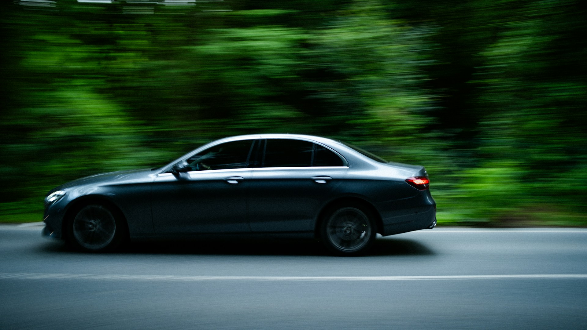 A black car driving down a street next to a forest