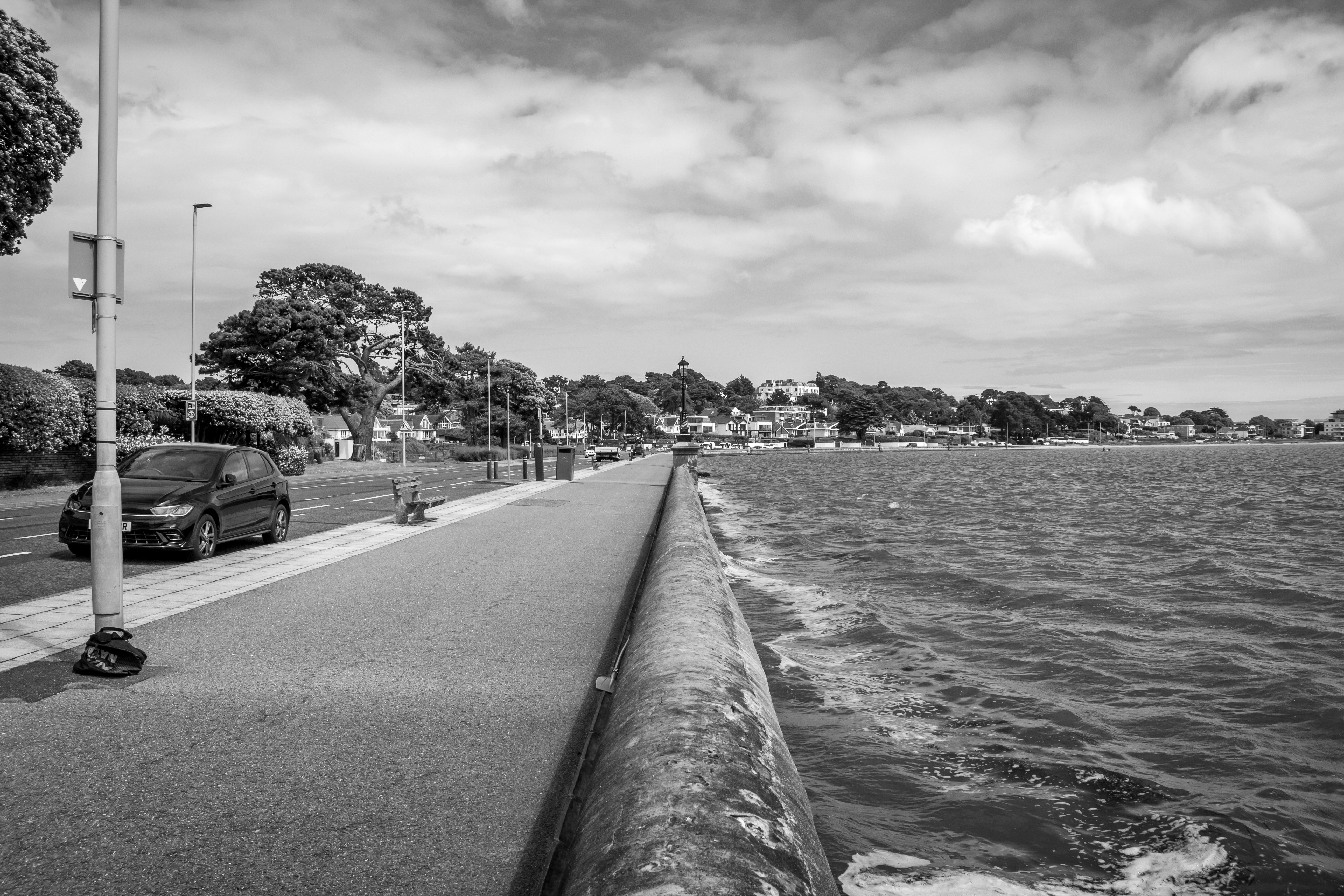A black and white photo of a street next to a body of water
