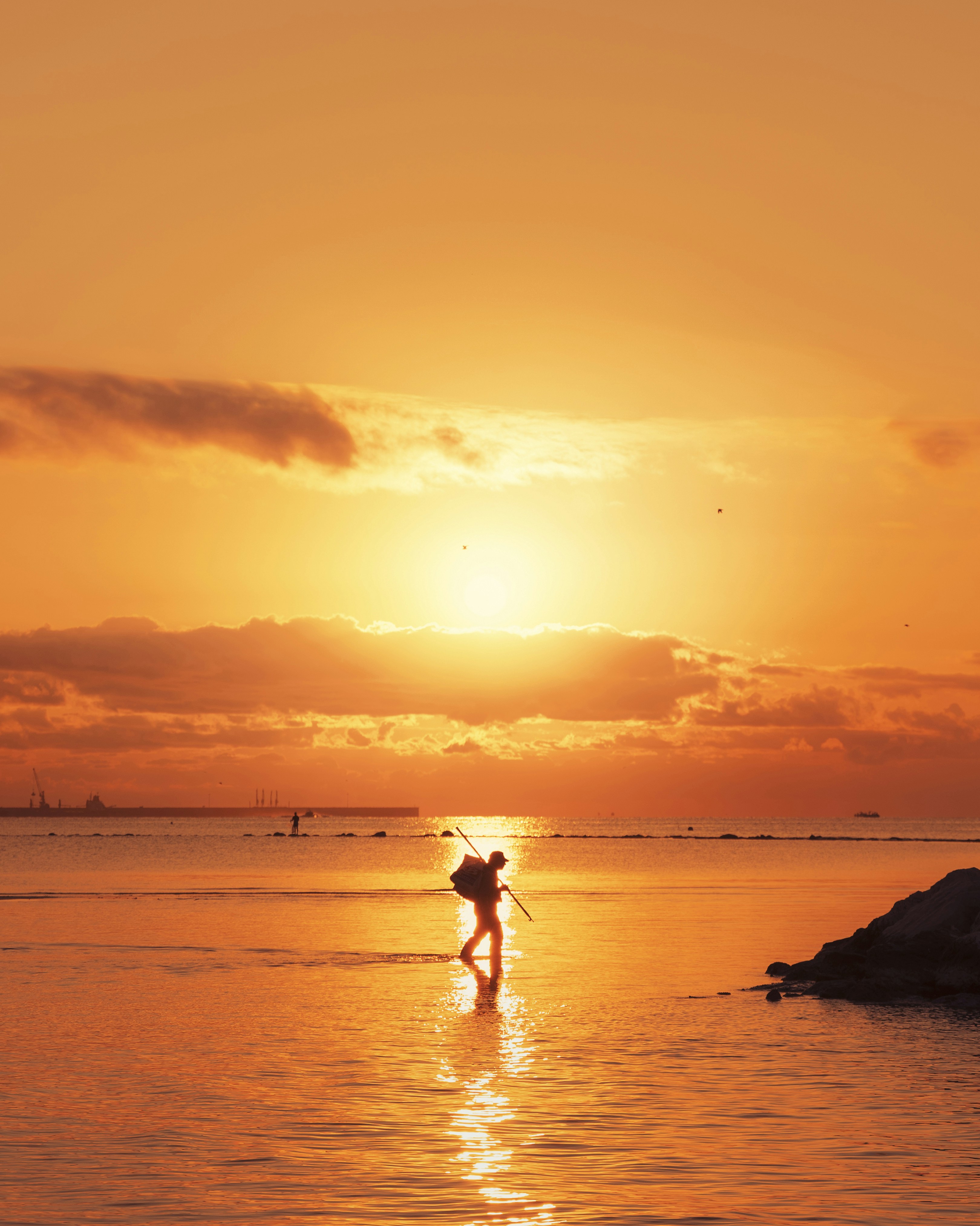 A person walking in the water at sunset