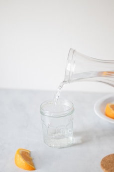 A pitcher pouring water into a glass filled with orange slices