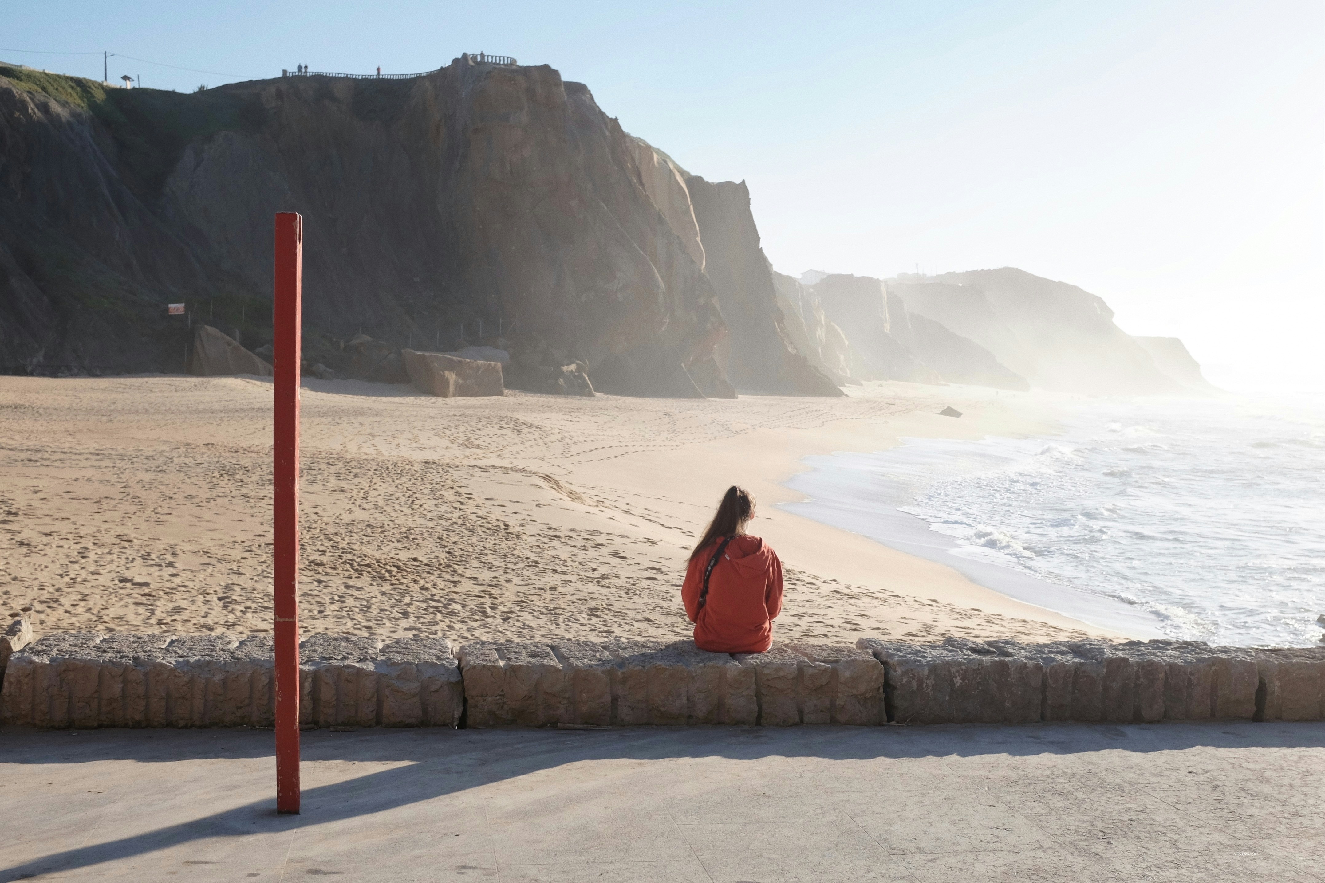 A woman sitting on the edge of a beach next to the ocean