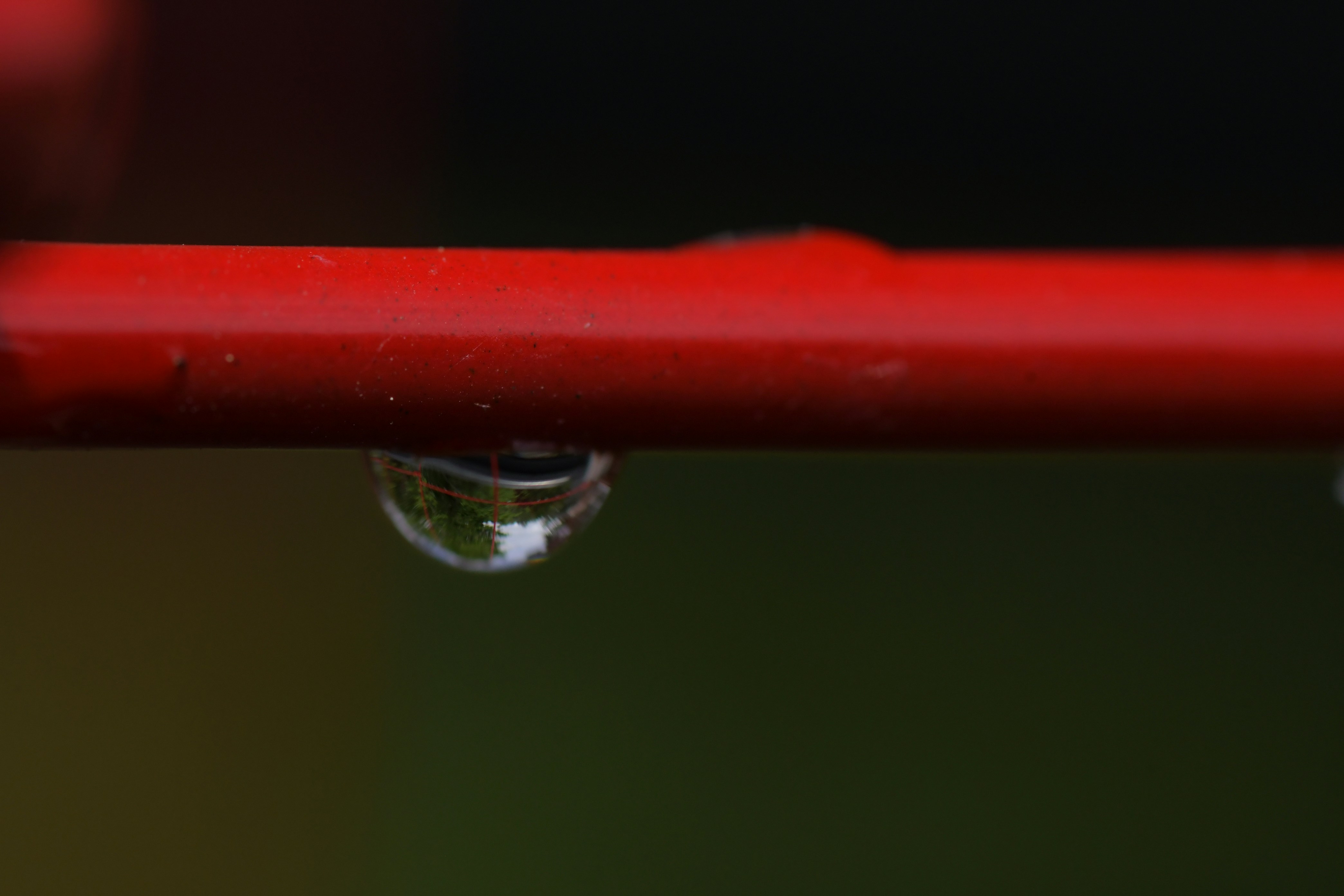 A close up of a red pipe with a drop of water on it