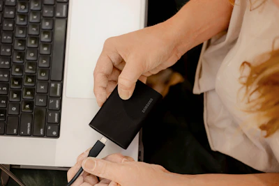 A person holding a cell phone in front of a laptop