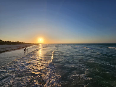 The sun is setting over the water at the beach