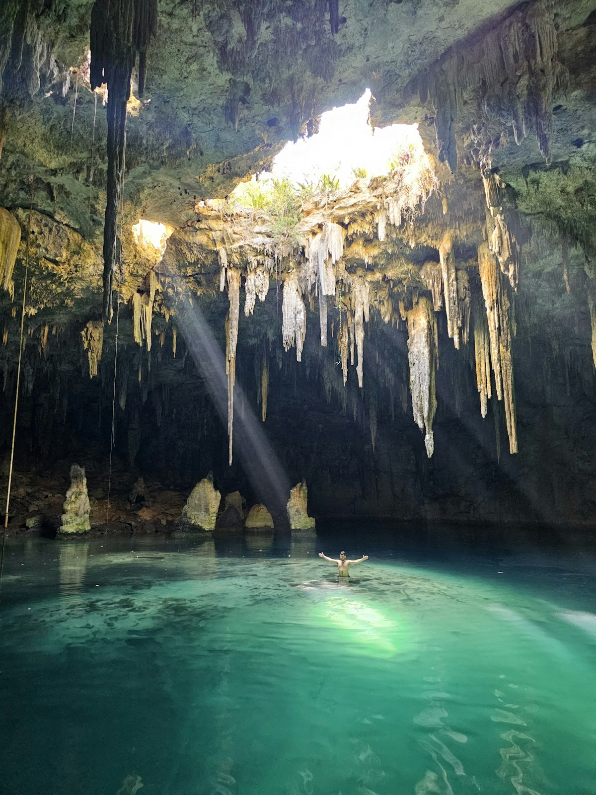 Underground cave cenote with sunlight streaming through an opening onto crystal clear water in Mexico
