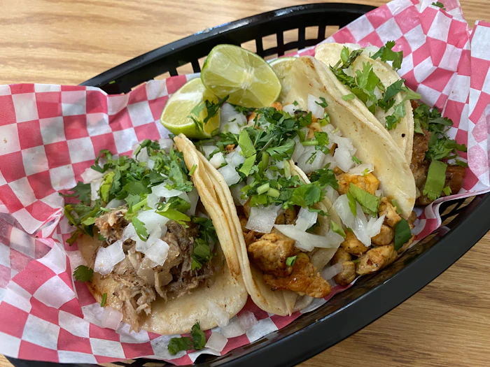 Three tacos in a basket with onion and cilantro