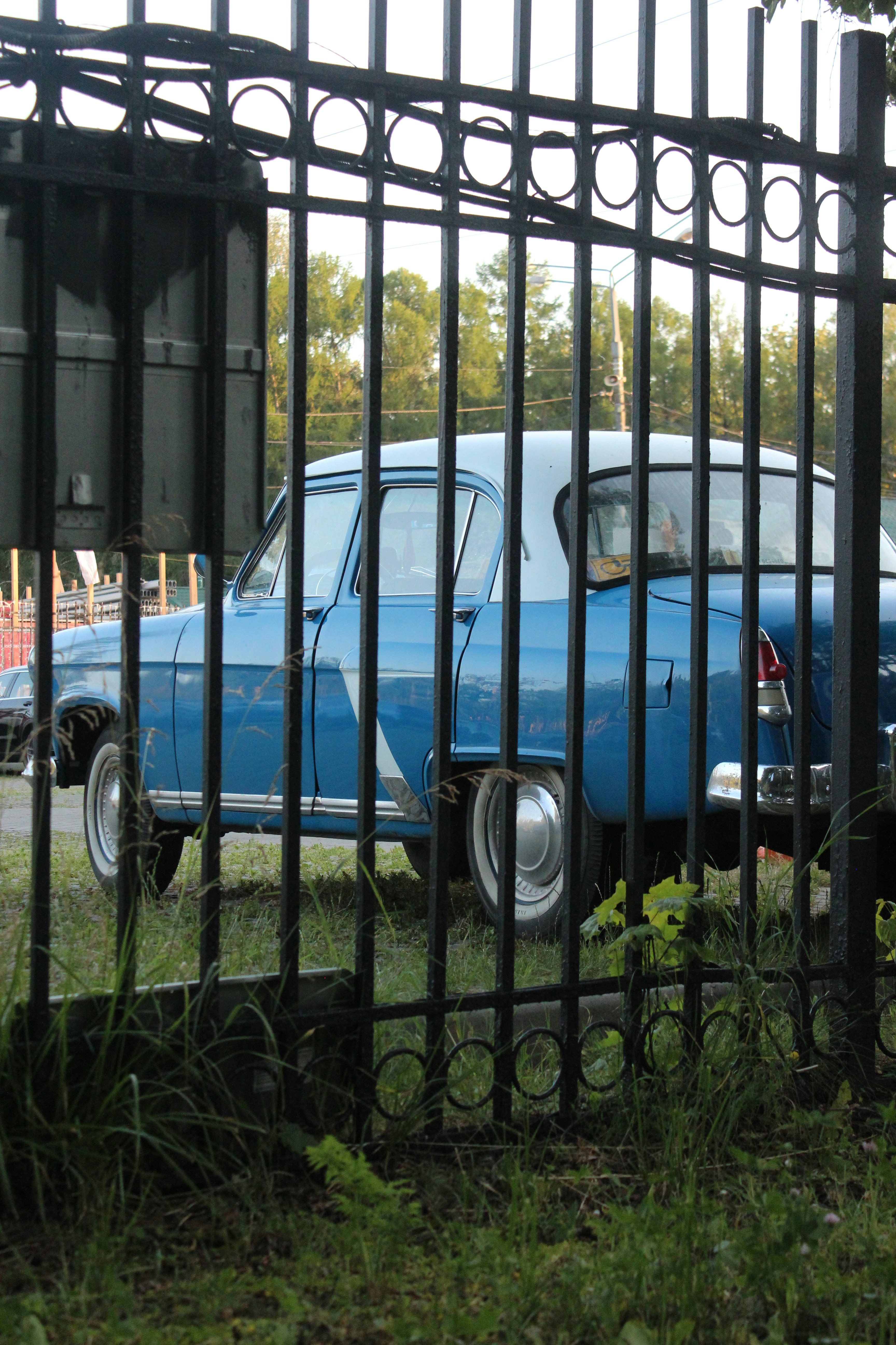 Una vecchia auto blu dietro una recinzione nera