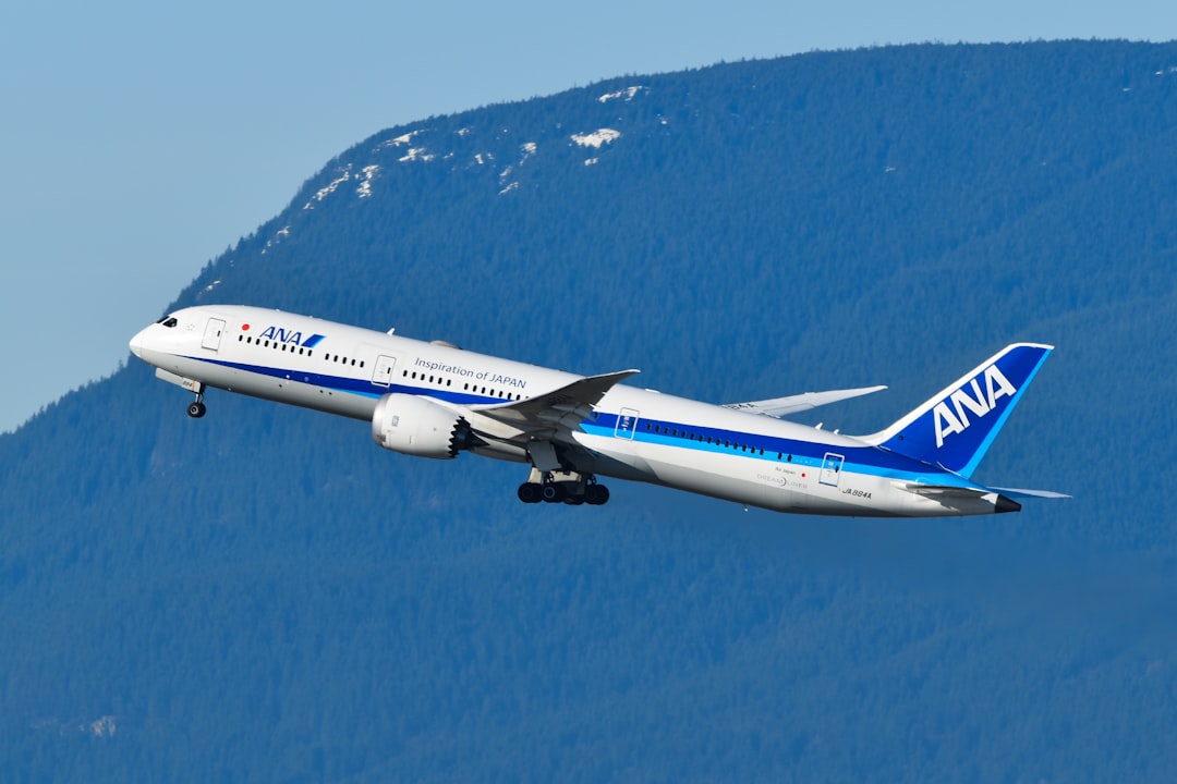 A blue and white airplane flying over a mountain, All Nippon Airways 787 departing Vancouver