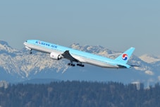 A blue and white airplane flying over a mountain range