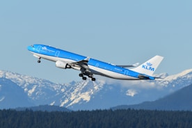A blue and white airplane flying over a mountain range