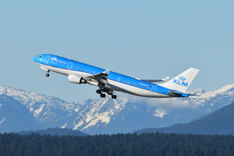 A blue and white airplane flying over a mountain range