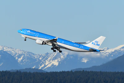 A blue and white airplane flying over a mountain range