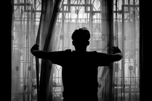 A black and white photo of a person standing in front of a window