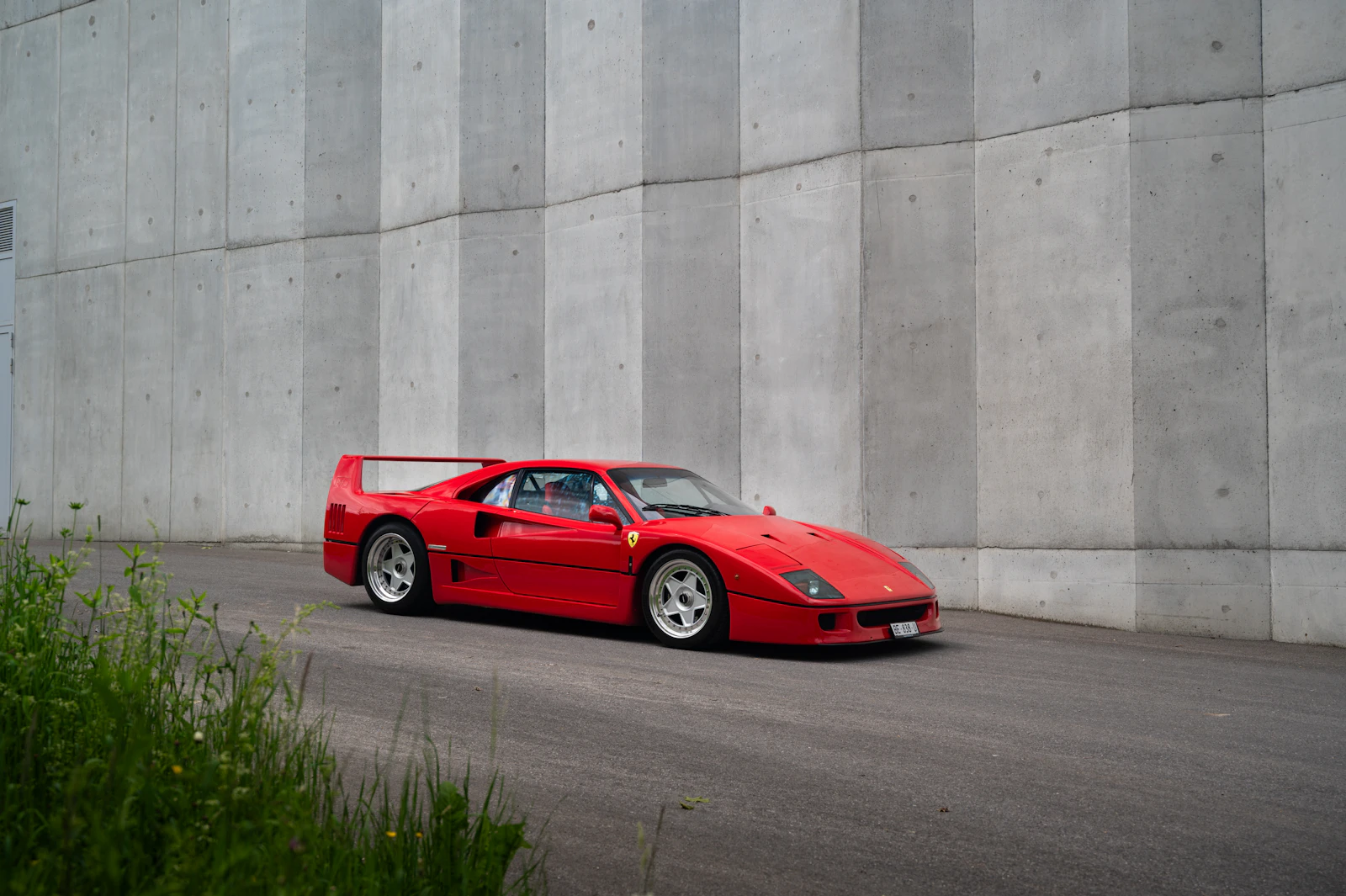 Red Ferrari F40 parked in front of a concrete wall