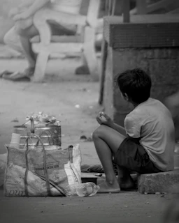 A boy sitting on the ground next to a bag