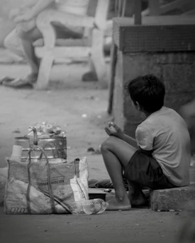 A boy sitting on the ground next to a bag