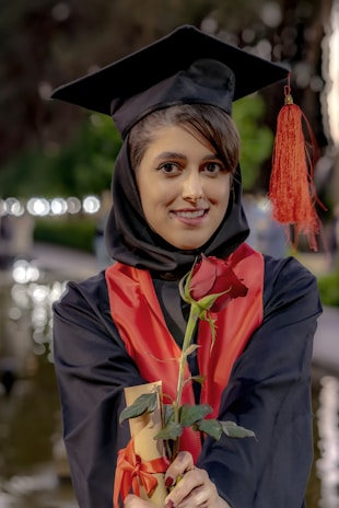 A woman in a graduation gown holding a rose