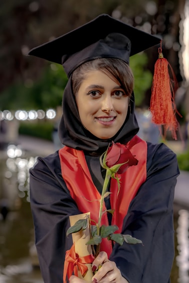 A woman in a graduation gown holding a rose