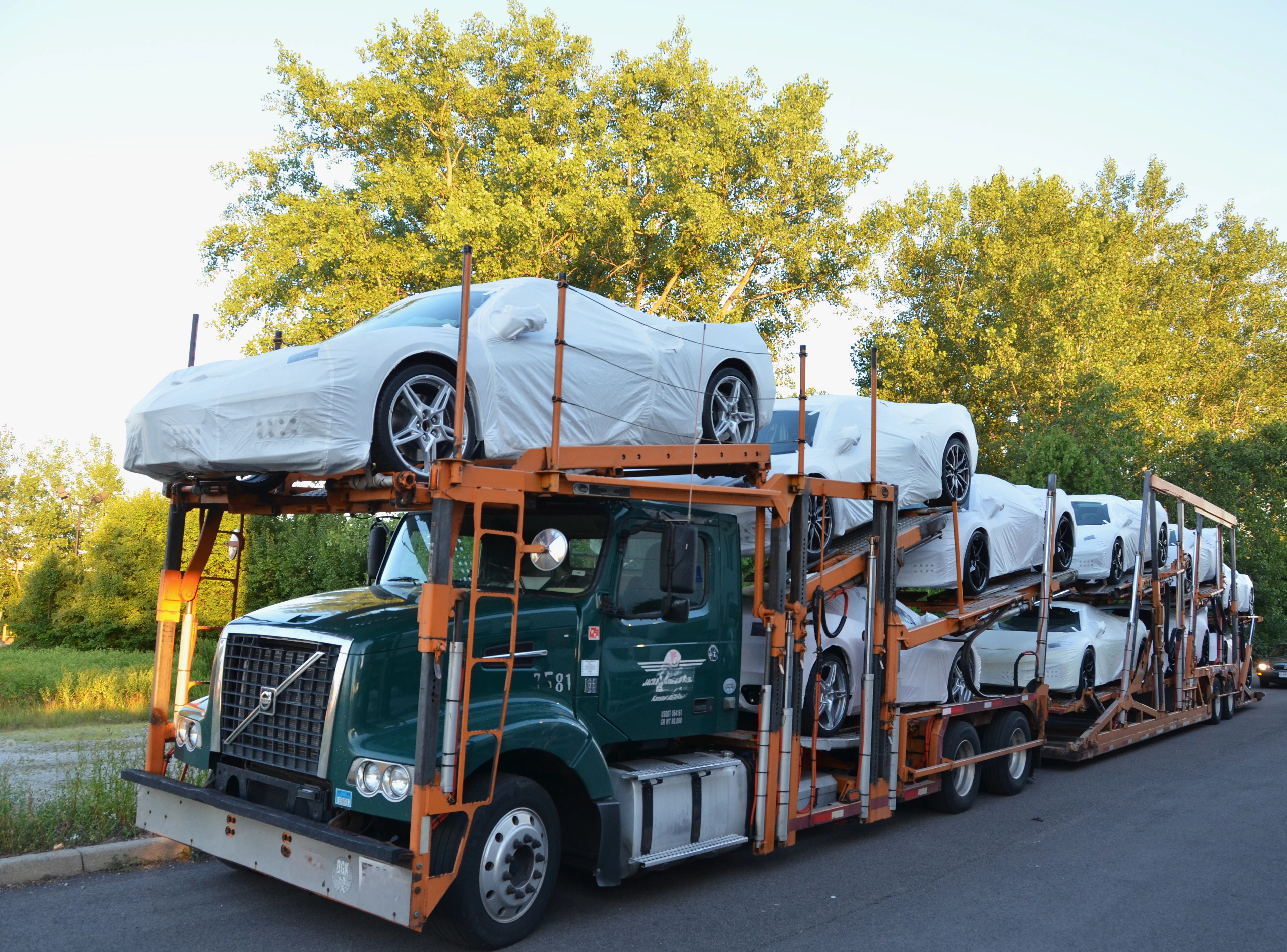 Car carrier truck transporting covered white sports cars
