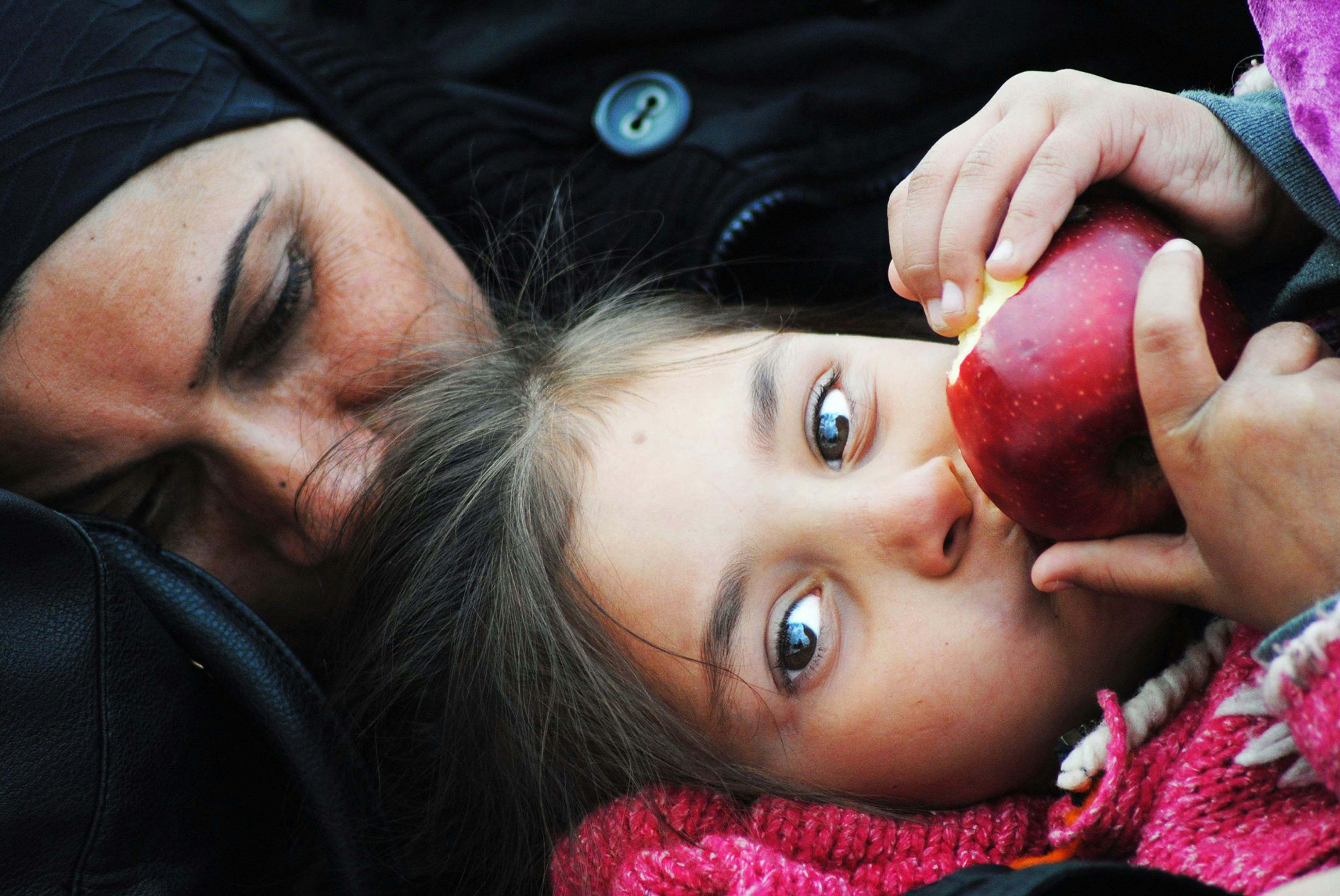 A man holding a little girl who is eating an apple