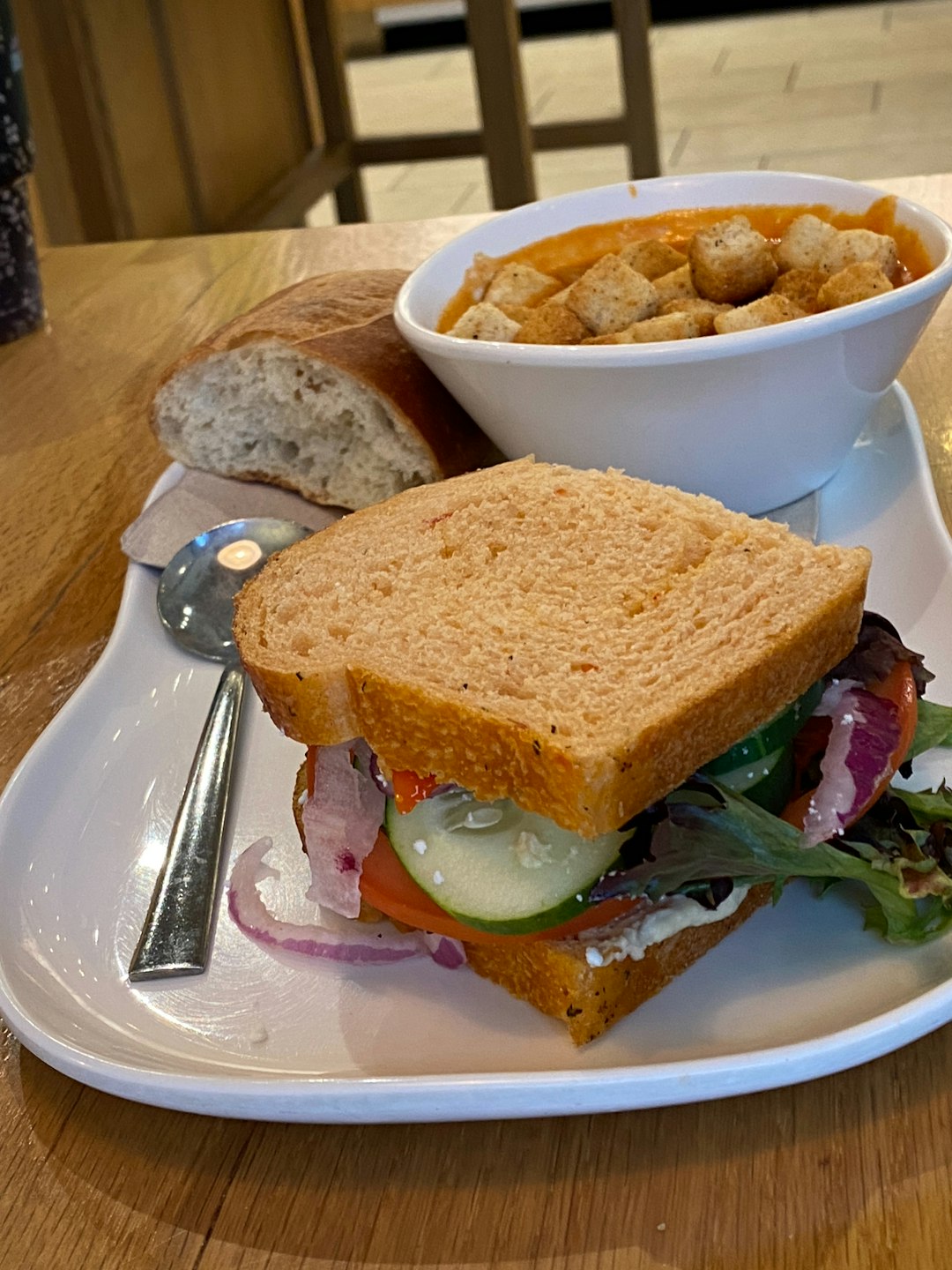 A white plate topped with a sandwich and a bowl of soup