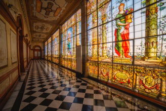 A long hallway with a checkered floor and large stained glass windows