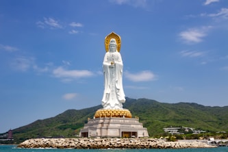 A large white statue sitting on top of a lush green hillside