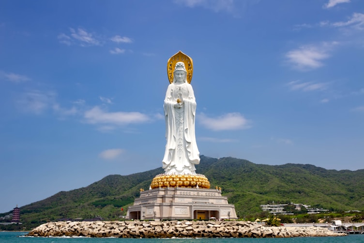 A large white statue sitting on top of a lush green hillside