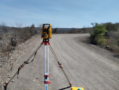 A yellow and black device is on a pole in the middle of a dirt road