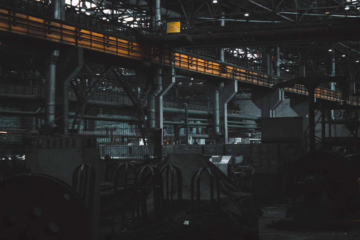 Interior de una planta industrial a oscuras, con el puente grúa amarillo cruzando la nave.