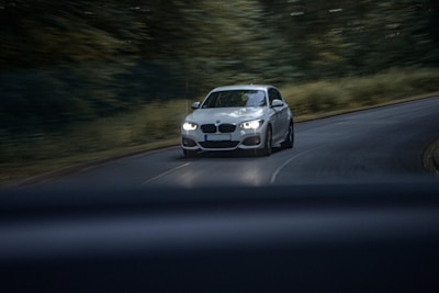 A white car driving down a road next to a forest