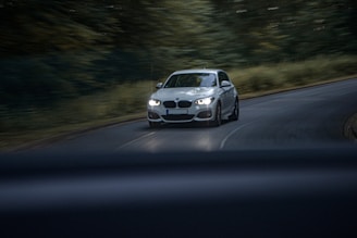 A white car driving down a road next to a forest