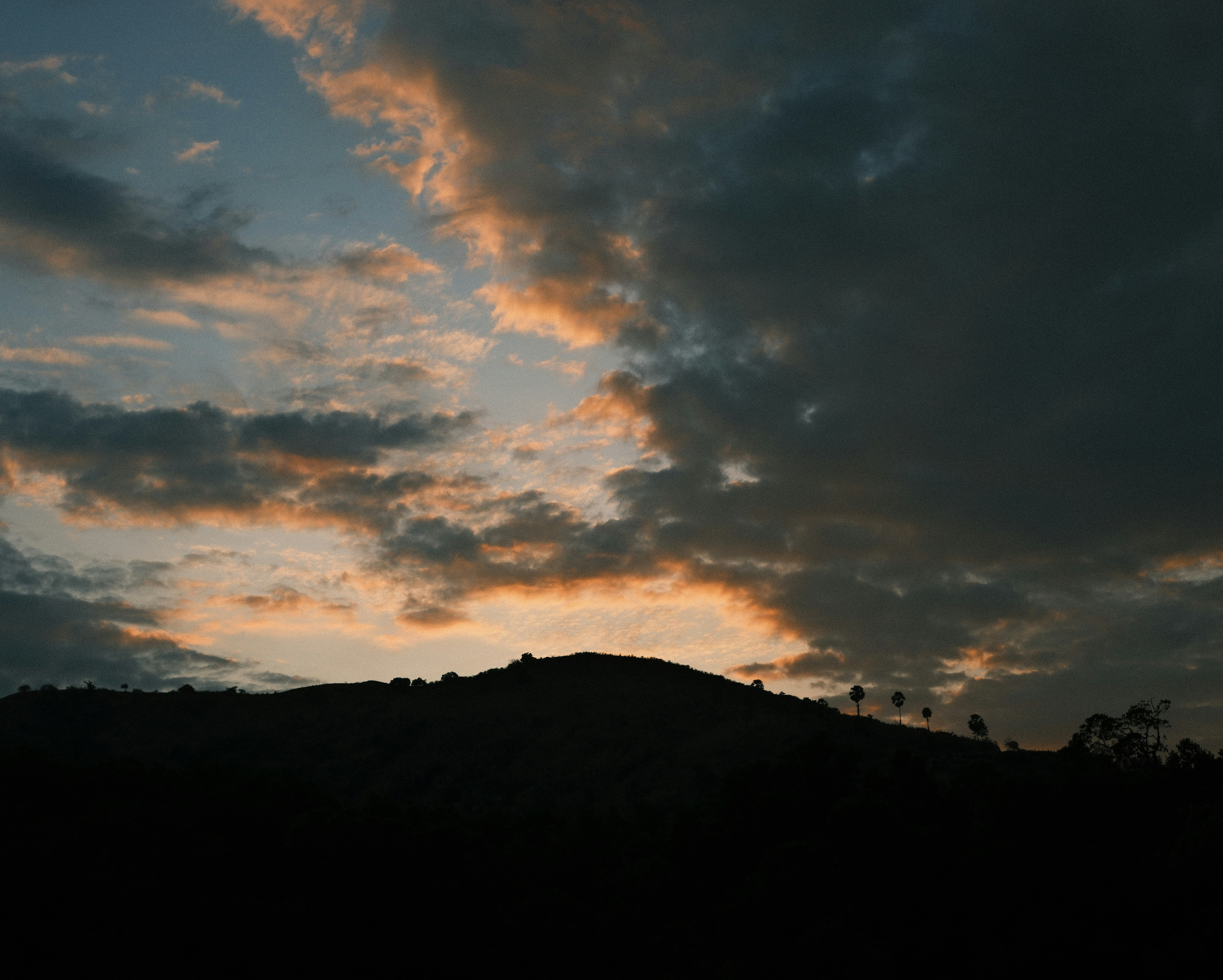 The sun is setting over a mountain with clouds in the sky