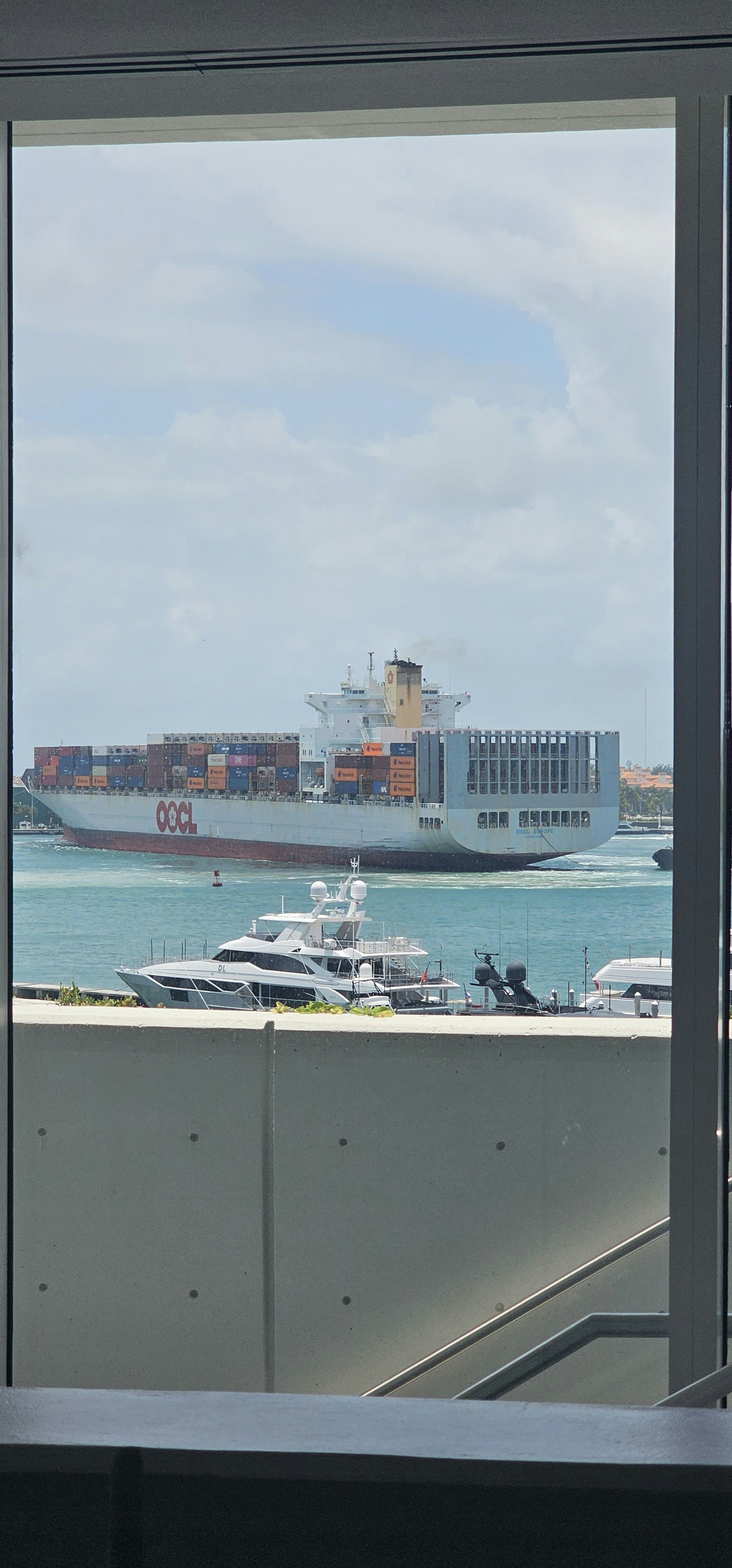 Ein großes Frachtschiff fährt an Yachten vorbei, die an einem Pier festgemacht sind.