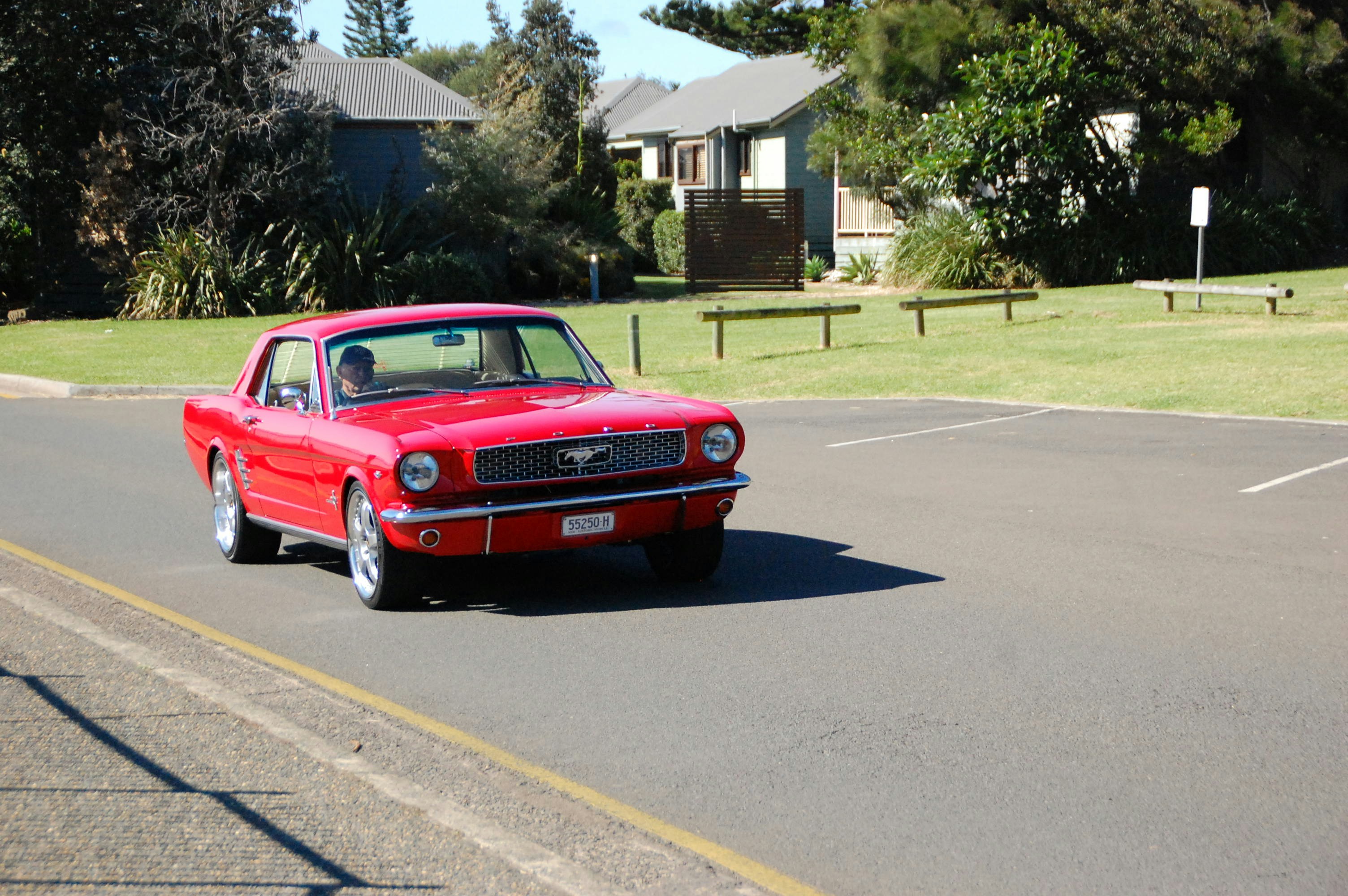 A red car driving down a street next to a park