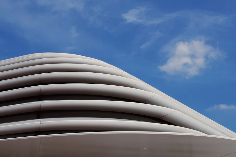 Modern curved architectural structure with wave-like design, predominantly white and gray, towering above